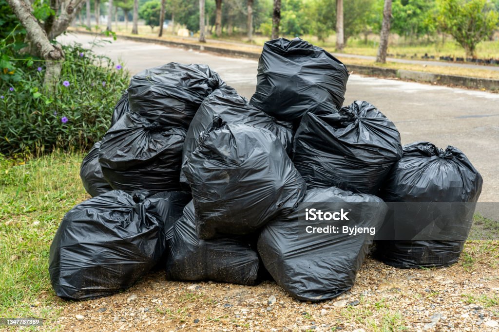 Black garbage bags on the road with green grass and plants background Asia, Thailand, Backgrounds, Bag, Black Color Garbage Stock Photo
