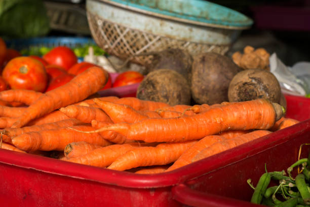 Fresh organic carrots on plastic tray for sale with other vegetables. Selective focus.