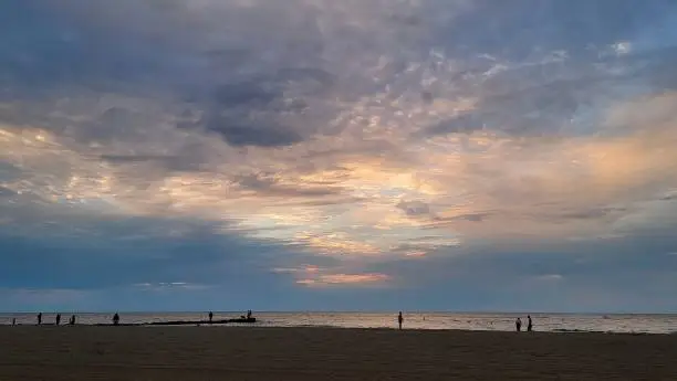 Ten individual silhouettes in various poses spread out along the shoreline with dramatic sky. Mood of connection to nature and self.