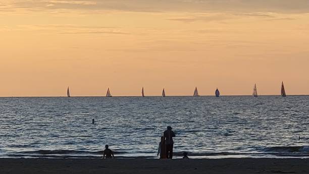 Three figures in silhouette with eight sailboats at sunset.
