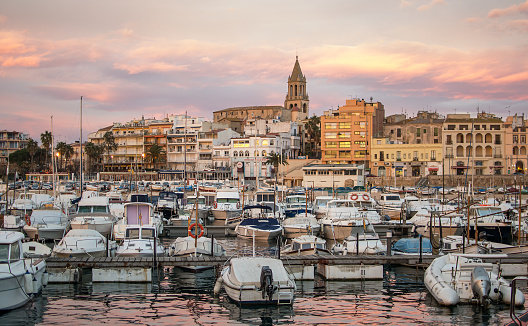 Sunset with the golden sky of the town of Palamós in Girona, Costa Brava, with its characteristic bell tower and the boats that are moored in the port