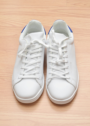 Closeup of a pair of generic, men's new white sneakers on hardwood flooring.