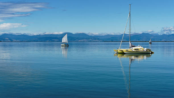 Motueka seafront, the Motueka sandspit in the background, Tasman region, New Zealand. Motueka seafront, a moored trimaran and a sailing dinghy, the Motueka sandspit in the background, Tasman region, New Zealand. motueka photos stock pictures, royalty-free photos & images