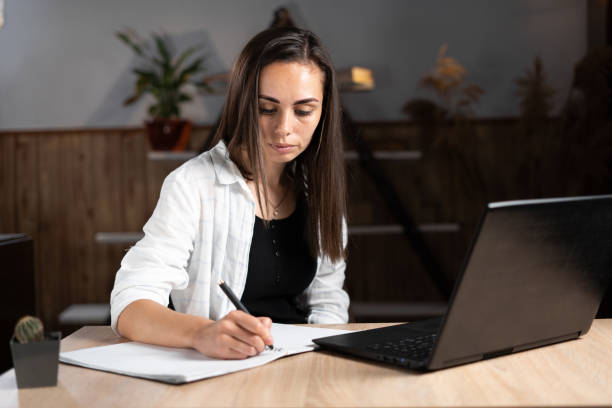 istock An adult college or university student learns remotely using a laptop and writing in a notebook. Online education or work at home. Caucasian girl writes homework in a notebook and studies 1347818722