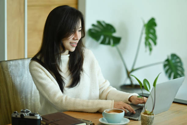 istock Thoughtful asian woman in white sweater using laptop computer at home. 1347818785