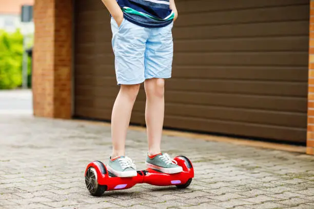 Close-up of kid boy on hover board. Child driving modern balance hoverboard. Excercise and sports for children, outdoor activity for young kids