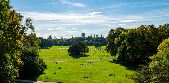 On October 14, 2021, looking to the Munich city center skyline from a hill in the English Garden in a autumn afternoon when many tourists and locals enjoy the sunny day to warm a little bit.