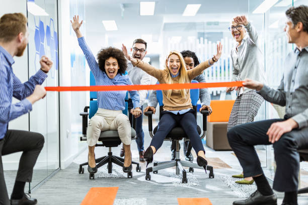 equipe de negócios alegre se divertindo durante a corrida de cadeiras no escritório. - office fun competition chair - fotografias e filmes do acervo