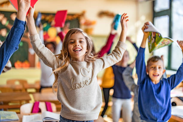 istock Playful elementary students jumping with raised arms in the classroom. 1347832313