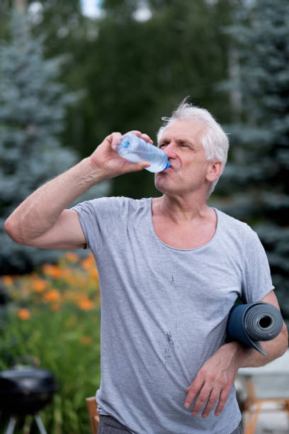 istock A handsome athletic fit gray-haired man drinks cool water from a bottle after a yoga class in the backyard. He holds a yoga mat in his hand 1347832626