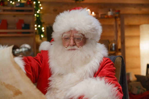 istock Serious Santa unfolding a scroll, sitting in his office, we see him in a a professional warm studio light 1347835012
