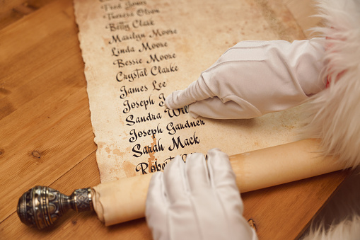 A top view on Santa's scroll with children's names and Santa's  hand in a white glove, pointing on one of the names