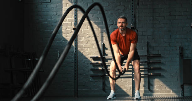 Shot of a handsome mature man standing and using battle ropes in the gym during his workout Never give up on a dream just because of the time HIIT Workout stock pictures, royalty-free photos & images