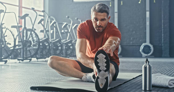 photo d’un bel homme mûr assis et s’étirant après s’être entraîné seul dans la salle de sport - action male only men mature men photos et images de collection