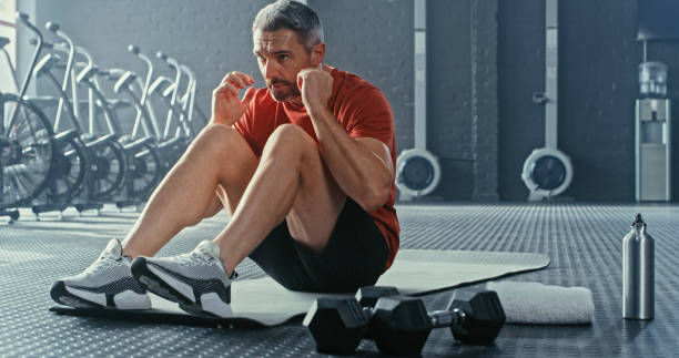 Shot of a handsome mature man doing sit-ups while working out in the gym alone Success is usually the culmination of controlling failure CRUNCHES stock pictures, royalty-free photos & images