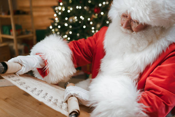 istock Santa Claus unfolding the scroll with children's names, sitting at his desk in a Study 1347837091