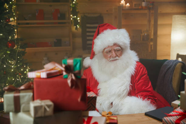 istock Santa sits at a table in his decorated office littered with gift boxes in a warm illumination 1347837297