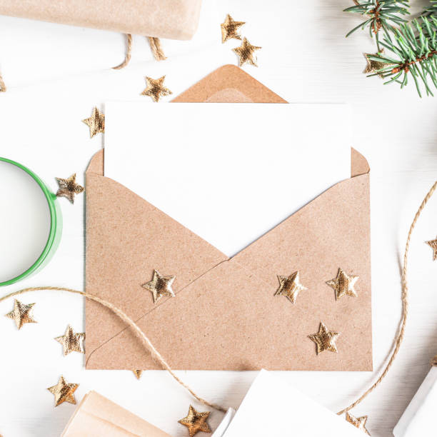 istock Open envelope with a white sheet for copy space on a white wooden background with Christmas decorations. Mockup for writing top view. 1347837321