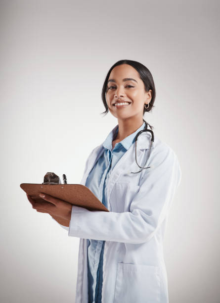 灰色の背景に立ちながらクリップボードを持っている女性医師のショット - 女医 ストックフォトと画像
