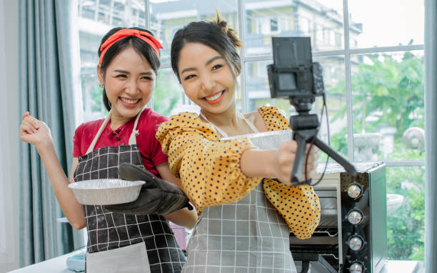 istock Two beautiful Asian women cooking food, making bread for breakfast and bakery while using tablet, streaming live video clip or taking selfie photo together with happiness and fun in kitchen at home. 1347838638