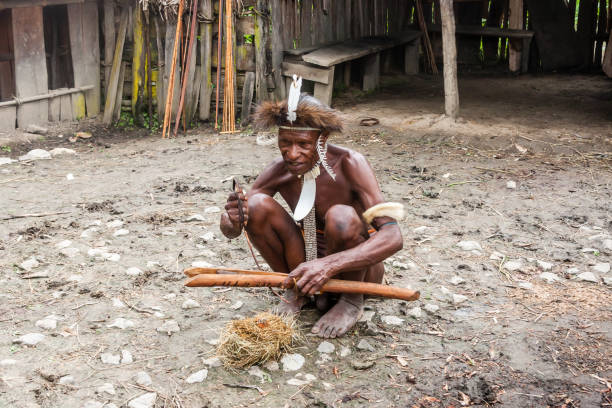 Man of the Dani tribe in a traditional dress kindles fire. Indonesian New Guinea Wamena, Indonesia - January 9, 2010: Man of the Dani tribe in a traditional dress kindles fire. Baliem Valley Papua, Irian Jaya, Indonesian New Guinea dani stock pictures, royalty-free photos & images