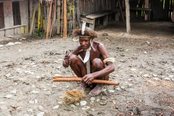 человек из племени дани в традиционной одежде разжигает огонь. индонезийская новая гвинея - dani стоковые фото и изображения