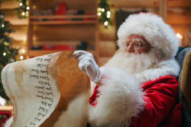 Santa Claus is sitting in a chair with a long paper scroll in his hands Santa Claus is sitting in an armchair, holding an ancient paper scroll in his hands and carefully reading the names on the list, checking if he has forgotten about someone finnish lapland stock pictures, royalty-free photos & images