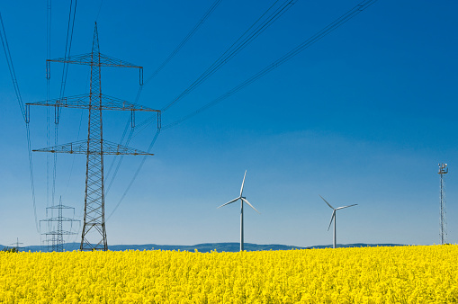 Electricity pylons, wind turbines and a mobile radio mast in the north of Frankfutrt in a flowering rapeseed field on the edge of the Wetterau