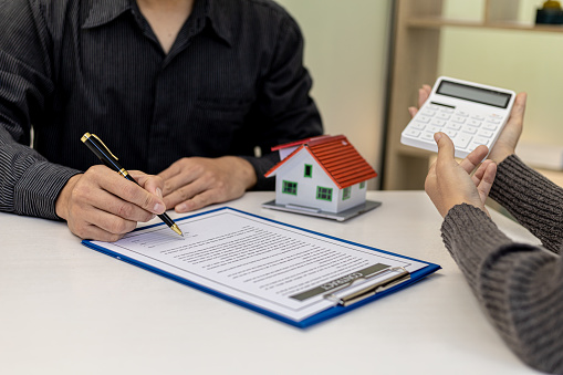 Real estate contract agreement concept. Buyer is signing house purchase contract with seller. Salesperson calculates house purchase cost and explains details on contract.