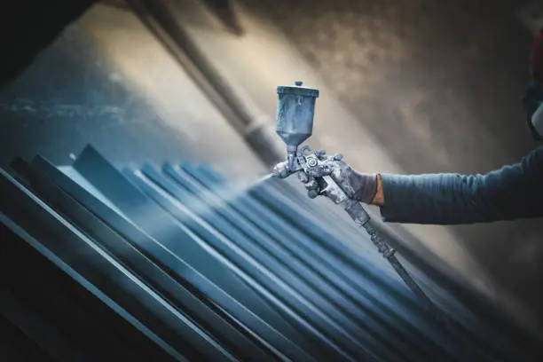 Photo of Man painting metal products with a spray gun