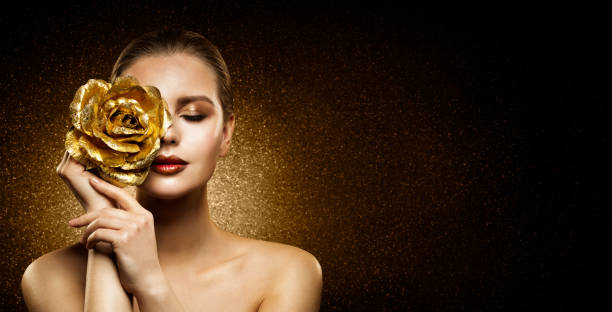woman beauty perfect glowing skin makeup. fashion model holding golden rose flower over face and covering closed eye. artistic glittering dark background with copy space - photography human hand portrait women imagens e fotografias de stock