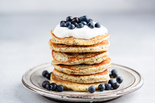 Poppy seed pancakes with yogurt and blueberries on a plate, Sweet breakfast pancakes, grey concrete background