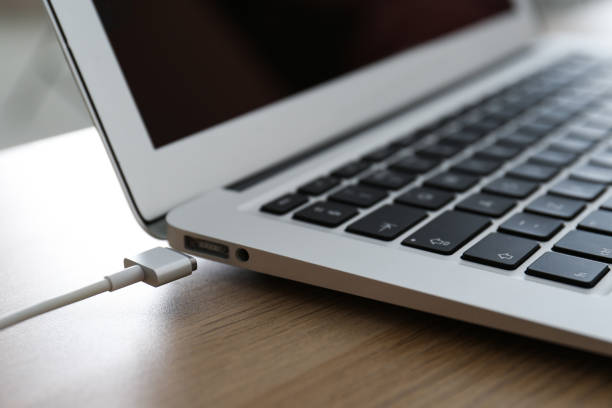 istock Modern laptop and charging cable on wooden table, closeup 1347853944