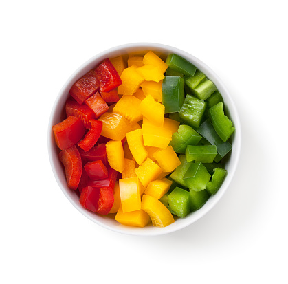 Cut pepper pieces in white bowl isolated on white background. Red, yellow and green chopped bell pepper. Top view
