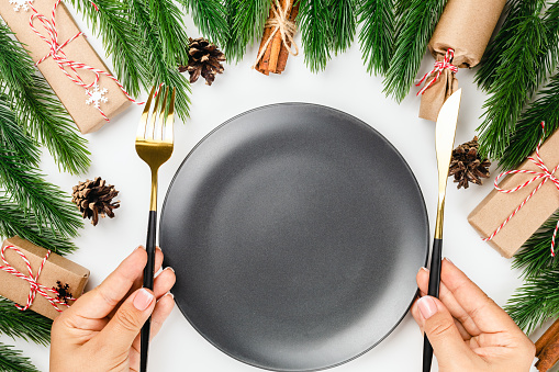 table set for Christmas party. Woman hands hold gold cutlery over black empty plate.