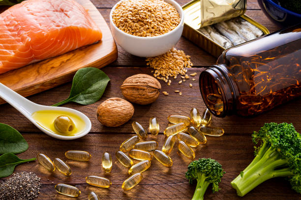 Heart care diet: Fish oil capsules and food rich in omega-3 Top view of many fish oil capsules spilling out from the bottle surrounded by an assortment of food rich in omega-3 such as salmon, flax seeds, broccoli, sardines, spinach, olives and olive oil. omega 3 photos stock pictures, royalty-free photos & images