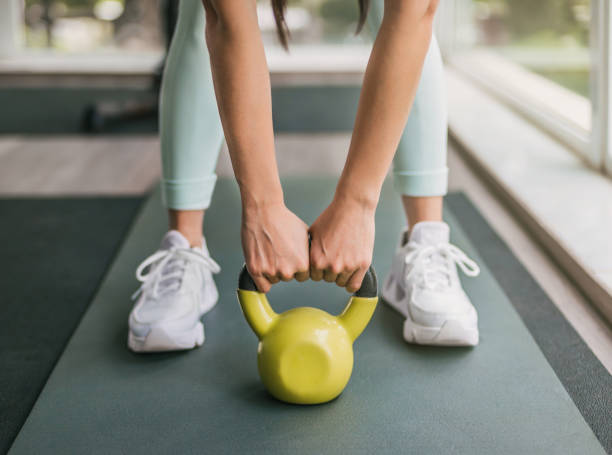 dziewczyna w zielonych legginsach podnosi żółtą kettlebell obiema rękami. ma na sobie białe trampki i stoi na piankowej macie. - gym yellow muscular build dumbbell zdjęcia i obrazy z banku zdjęć