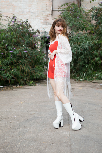 Boho-style young woman with long hair wearing a lace shawl, red dress, and white platform boots