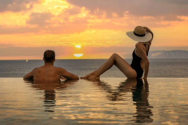 honeymoon vacation - couple enjoying romantic sunset in infinity pool at luxury resort - honeymoon beach swimming pool couple imagens e fotografias de stock