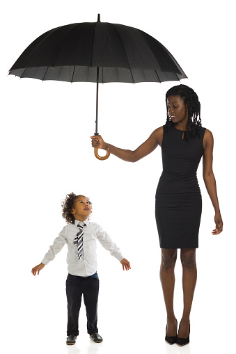 Elegant african woman in mini dress and high heels is standing and holding umbrella above lottle boy. Full length on white background.