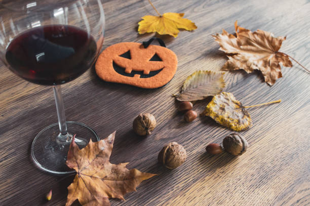 halloween stillleben. glas rotwein, herbstlaub und kürbisfigur mit nüssen. halloween deko auf holztisch. gruselige dekoration. oktober stillleben. - glass autumn halloween food stock-fotos und bilder