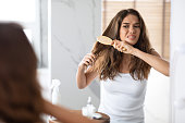 Desperate Woman Brushing Dry Tangled Hair With Hairbrush At Home