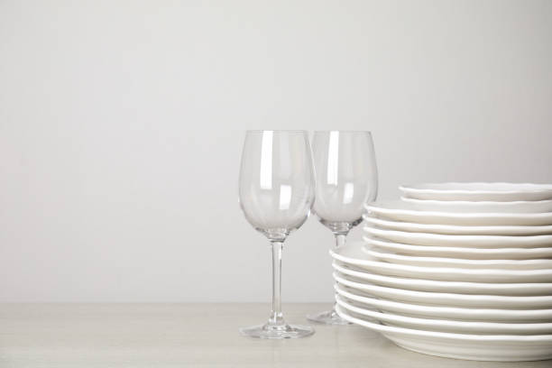 istock Stack of clean plates and glasses on table against white background. Space for text 1347868563