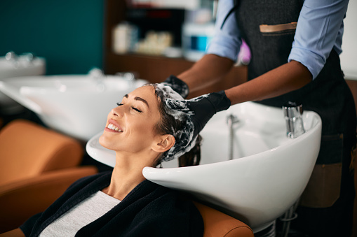 Smiling woman getting head massage while washing hair at hair salon.