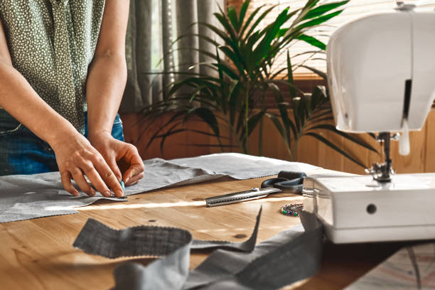 Woman taking measurements on the linen fabric. Seamstress sewing on the sewing machine in small studio. Fashion atelier, tailoring, handmade clothes concept. Slow Fashion Conscious consumption Woman taking measurements on the linen fabric. Seamstress sewing on the sewing machine in small studio. Fashion atelier, tailoring, handmade clothes concept. Slow Fashion Conscious consumption atelier fashion stock pictures, royalty-free photos & images