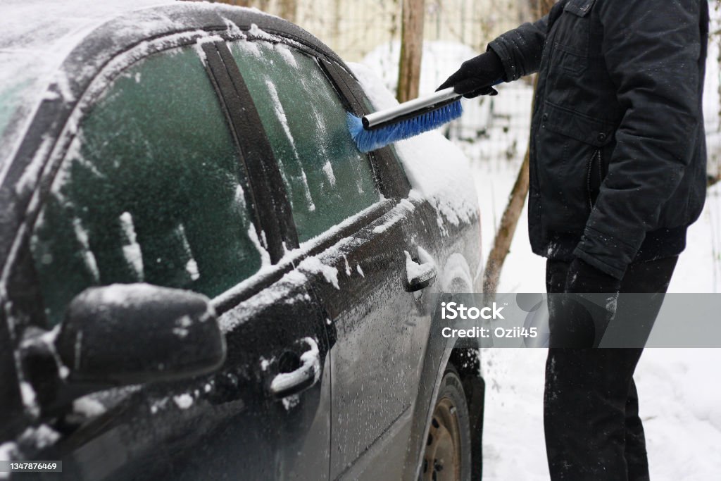 A man cleans the car from snow with special brushes. A car covered with snow. A man cleans the car from snow with special brushes. Accidents and Disasters Stock Photo