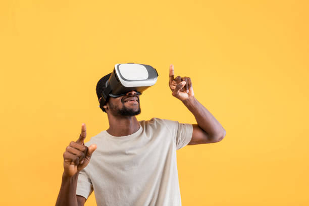 istock African american guy in modern VR glasses exploring virtual reality, moving his hands over yellow background 1347878637