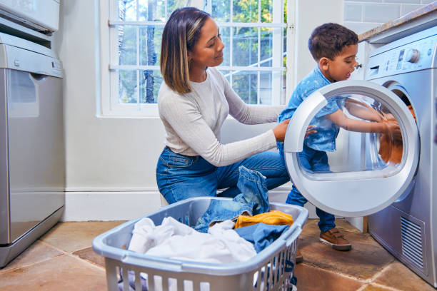 scatto di un ragazzino che aiuta sua madre a caricare il bucato in lavatrice - fare il bucato foto e immagini stock
