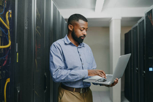 istock Shot of a young man using a laptop while working in a server room 1347879797