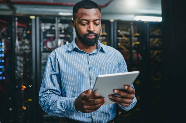 istock Shot of a young man using a digital tablet while working in a server room 1347879799